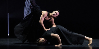 Two male ballet dancers together on stage in black clothing
