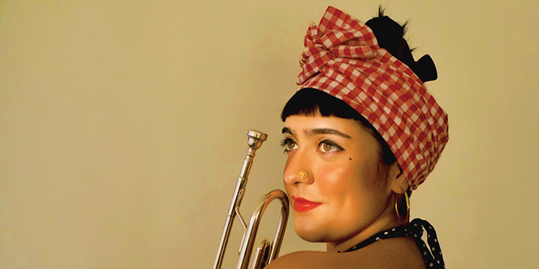 Olivia Cuttill holding a trumpet, wearing a black halter top with dark hair up in a red and white polka dot bandana